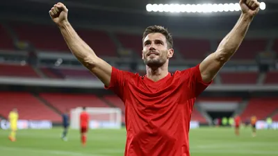 Photorealistic shot of a mid-20s male football fan, athletic build, wearing a solid red jersey, celebrating with arms...